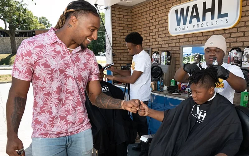 A man fist bumps a kid getting a haircut at the mobile barbershop.