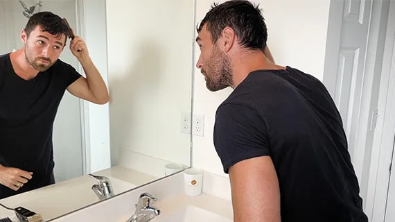 A man in a black shirt dampening and combing his hair as he looks in a mirror.