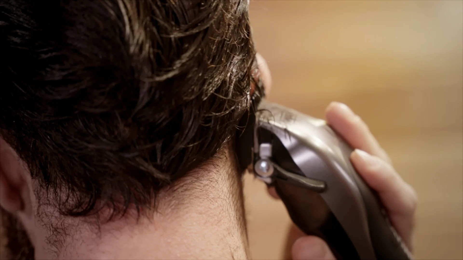 A close up of a man using a Wahl hair clipper to cut the back of his head.