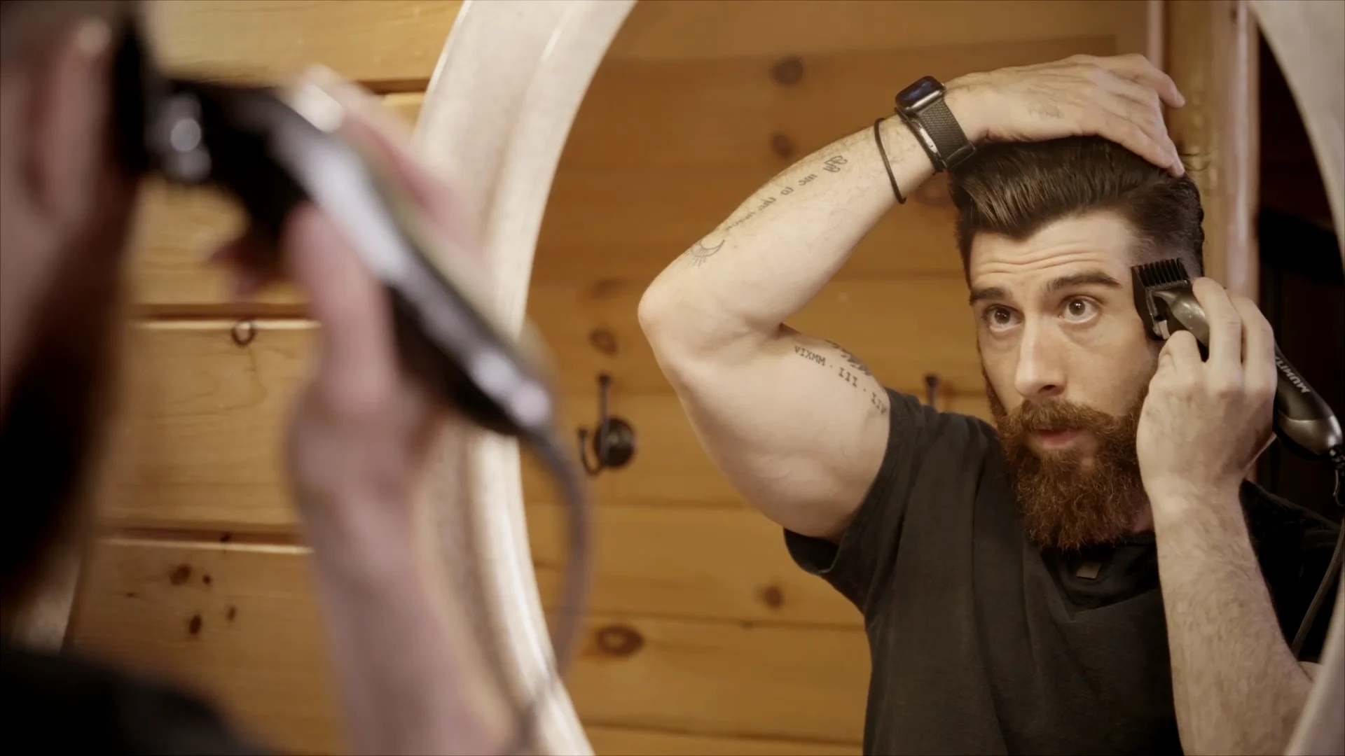 A bearded man using a Wahl hair clipper to cut the side of his head.