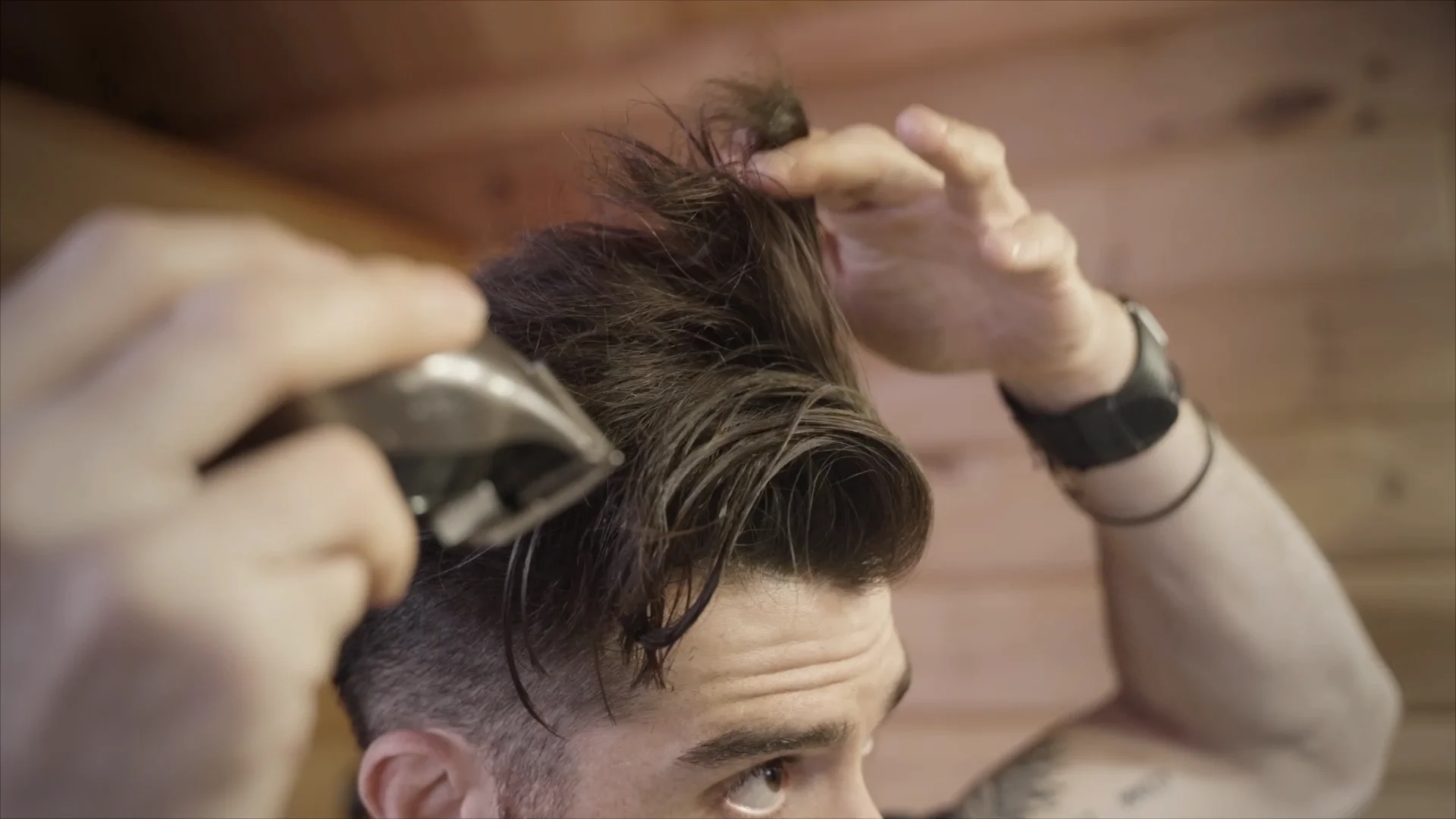 A man using the clippers over fingers technique to trim the top of his head.