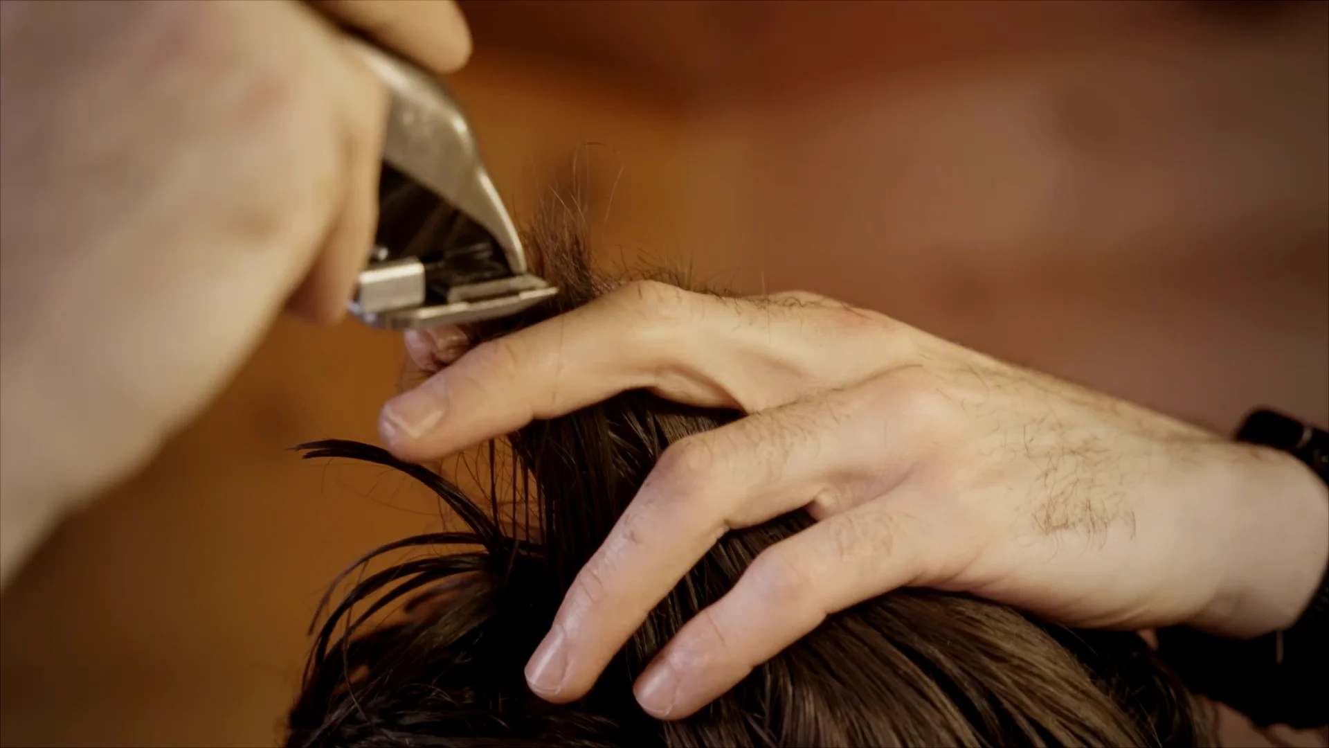 A close up of a man using the clipper over fingers technique and a Wahl hair clipper to trim the top of his head.