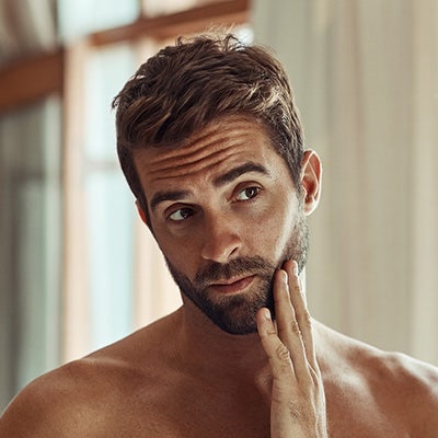 A man evaluating his beard while looking at himself in the mirror. 