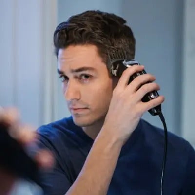 A man looking into the mirror as he uses a Wahl hair clipper to trim the side of his head. 
