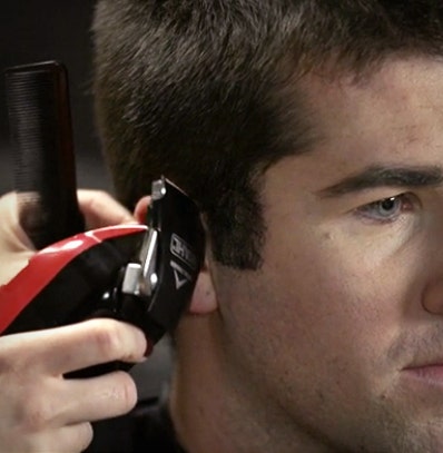 A man getting a haircut touch up around the arch of his ear.