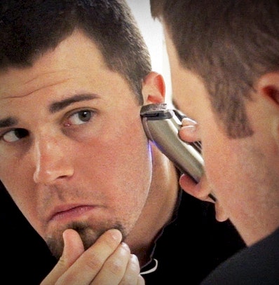 A man touching up his sideburns after giving himself a haircut.