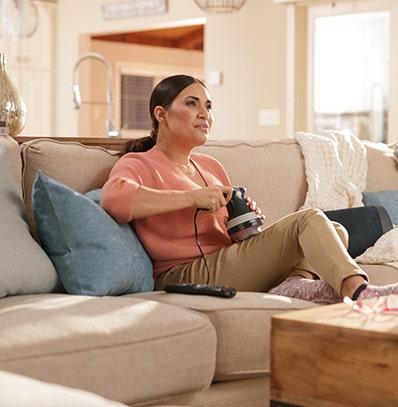 A woman using a Wahl handheld massager on her quad or upper thigh. 