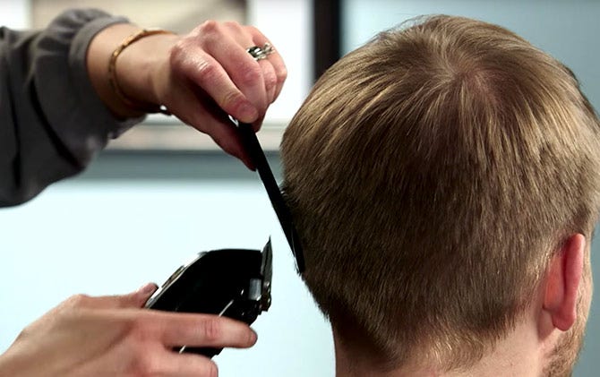 Someone using a comb as a haircutting guide on the back of a man's head. 