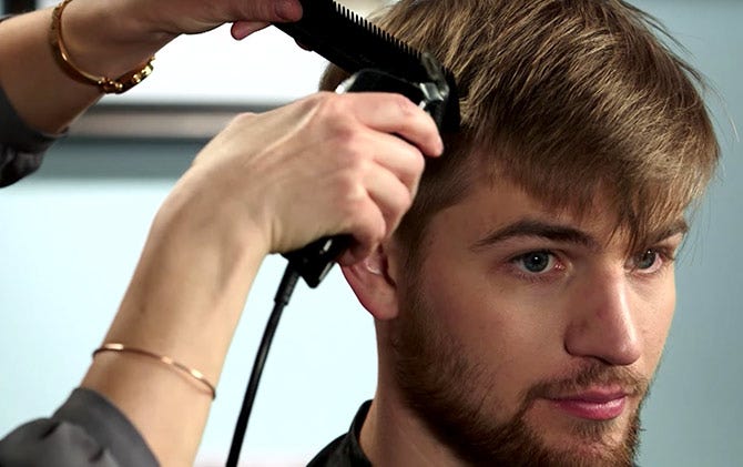 Someone using a comb as a haircutting guide on the side and front of a man's head. 