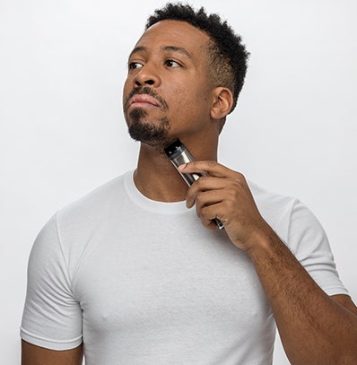 A man cleaning up stray hairs around his mouth and lips with a Wahl trimmer. 