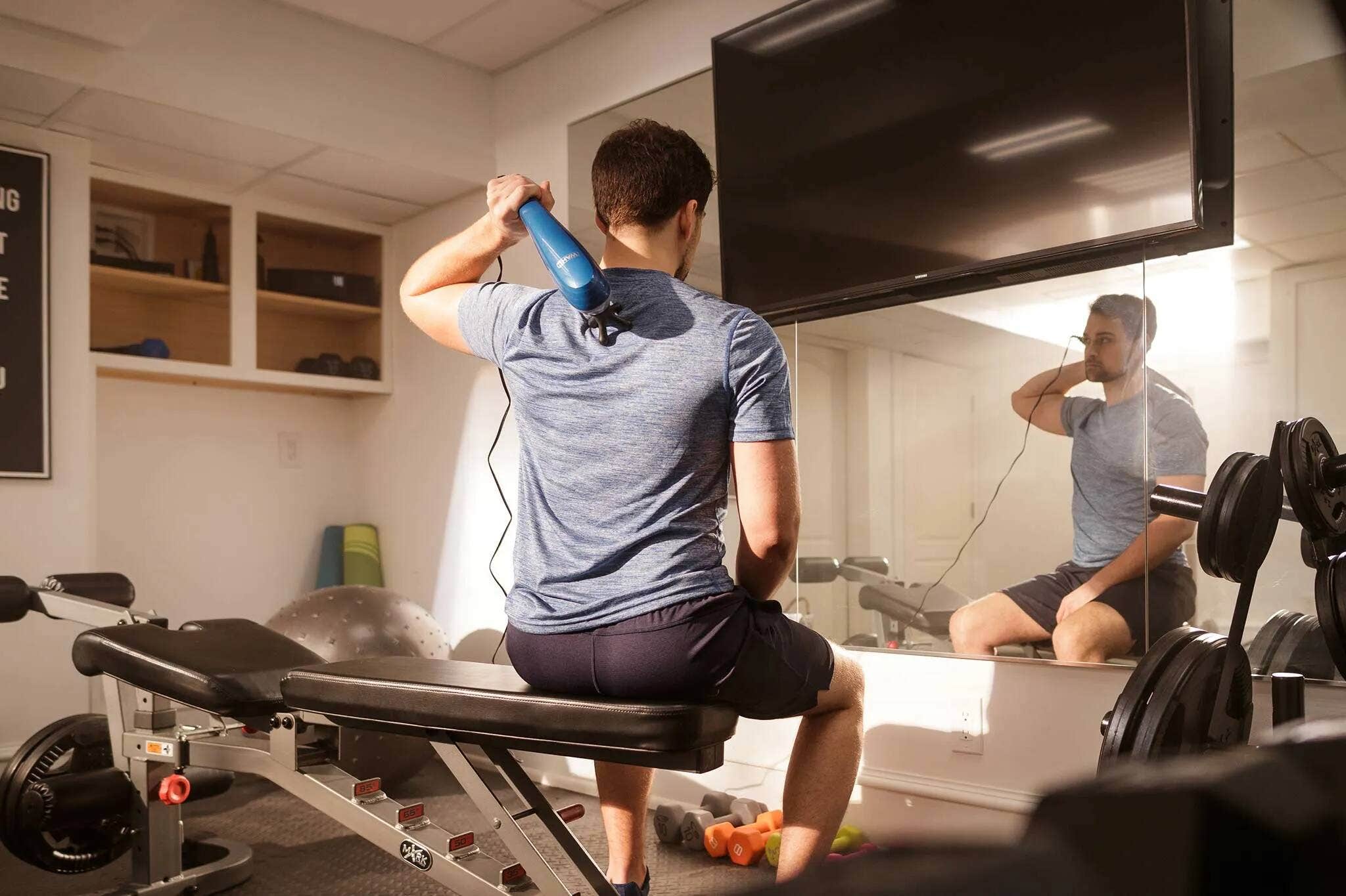 A man using a Wahl handheld massager on his upper back after a workout. 