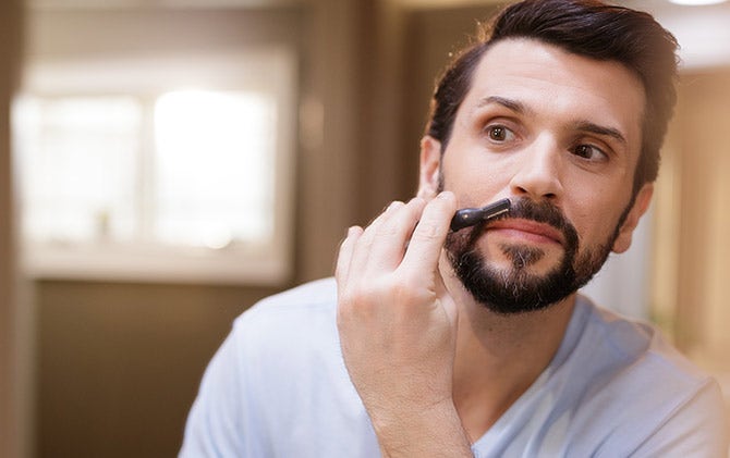 A man using just enough pressure to trim away hair from his mustache with a Wahl trimmer and attachment head. 