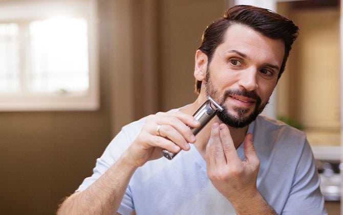 A man cleaning up the facial hair around the mouth area with a Wahl trimmer. 