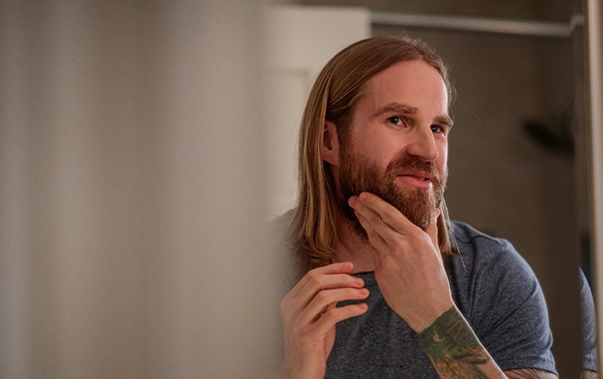 A man looking in the mirror admiring his groomed full beard.