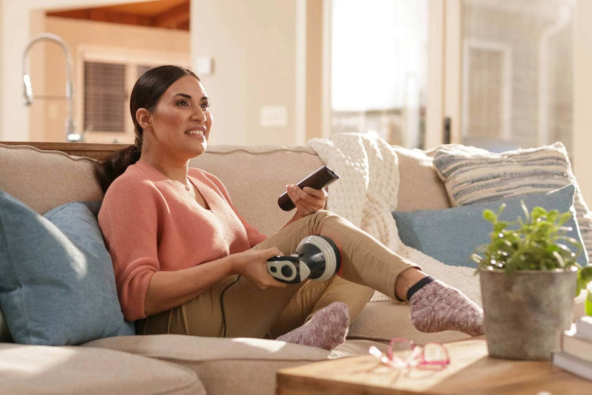 A woman using a Wahl handheld deep rolling shiatsu massager on her upper leg and thigh.