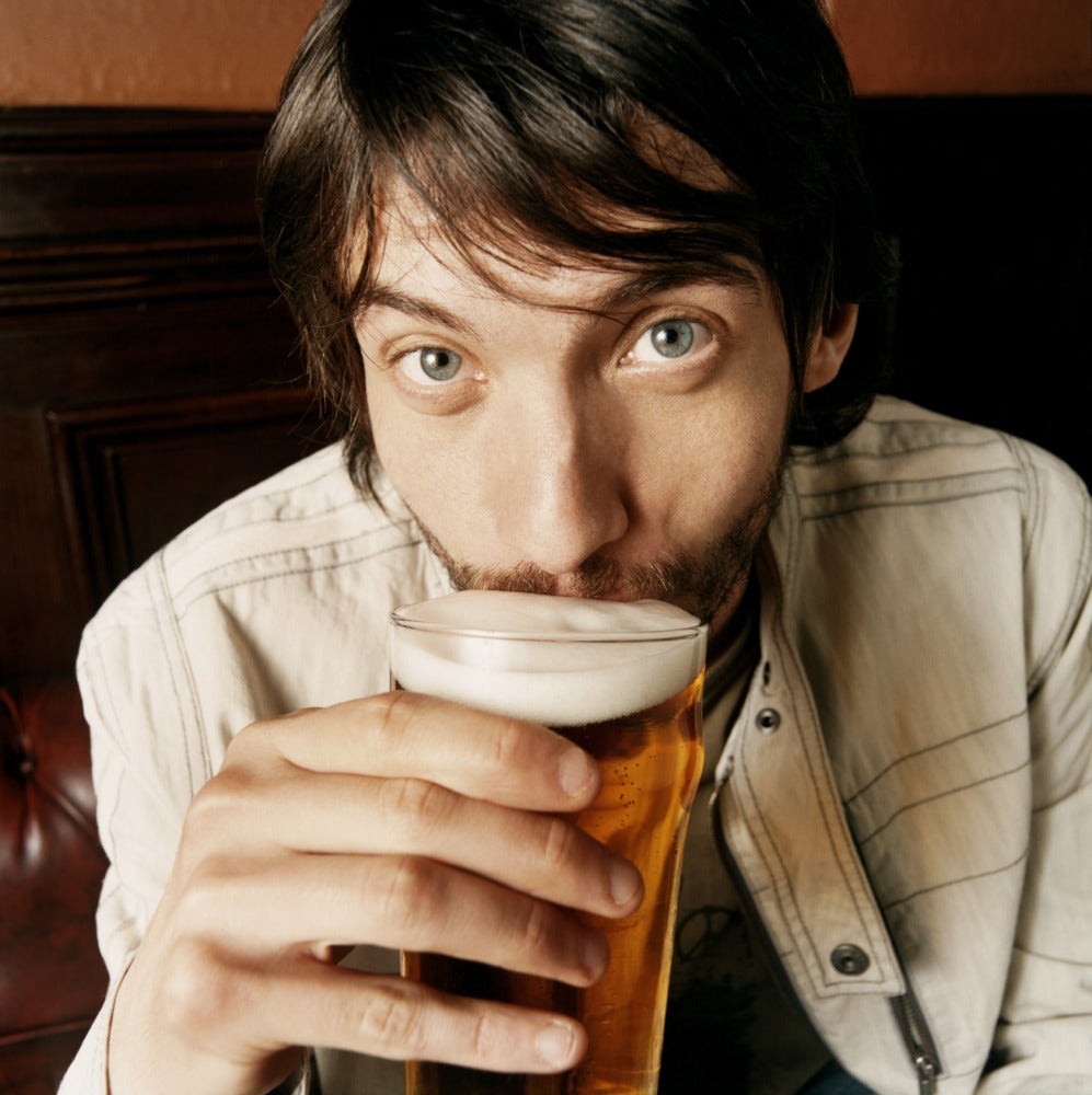 A close-up of a man sipping a beer.